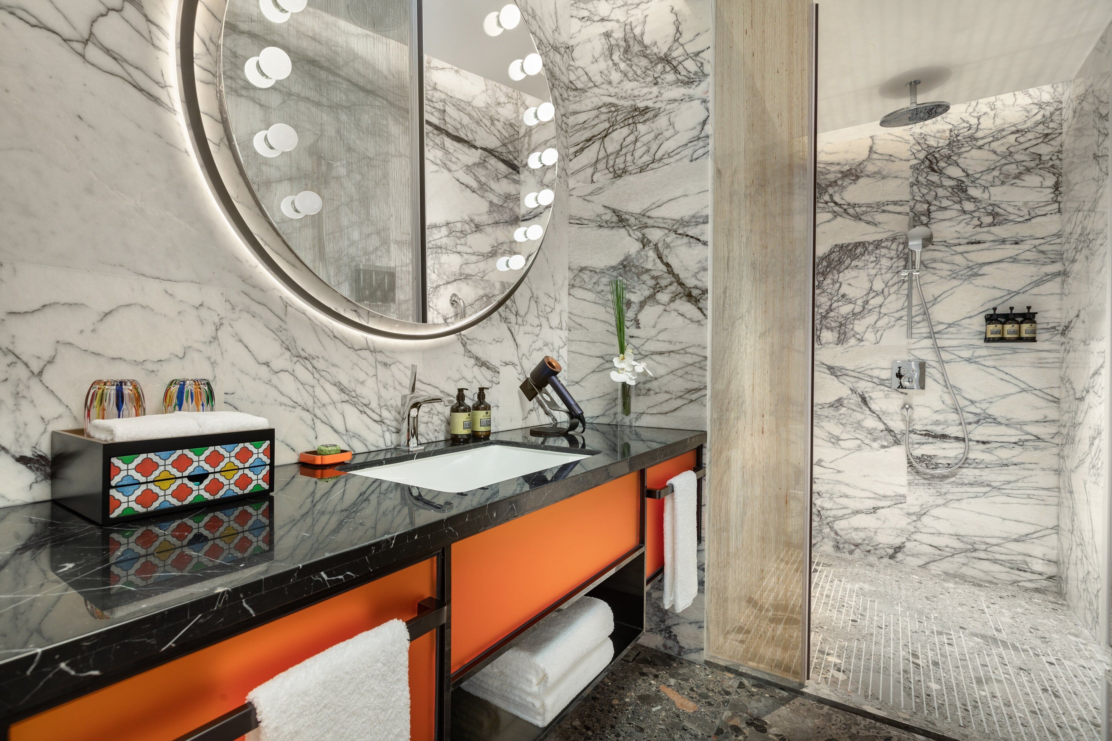 A bathroom with a marble wall, a sink with a mirror, and a shower area.