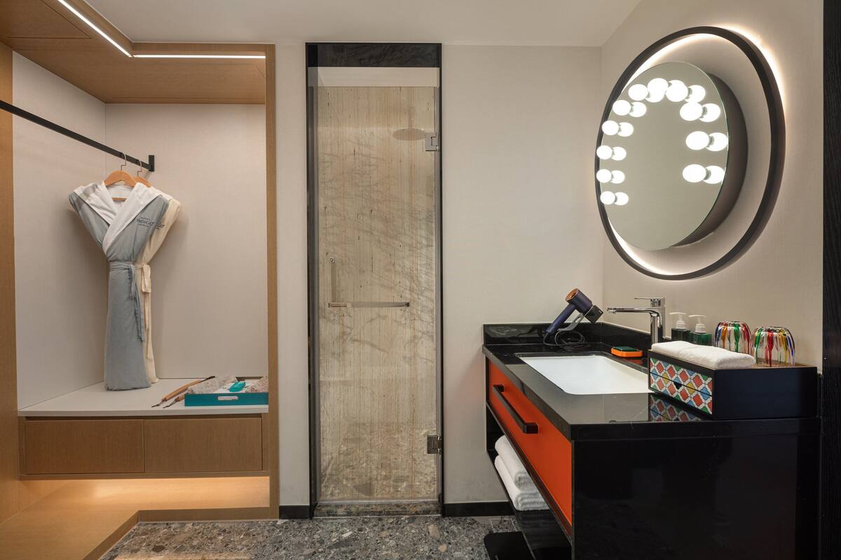 Un baño moderno con tocador, un espejo grande con luces, un perchero para toallas y una zona de ducha.