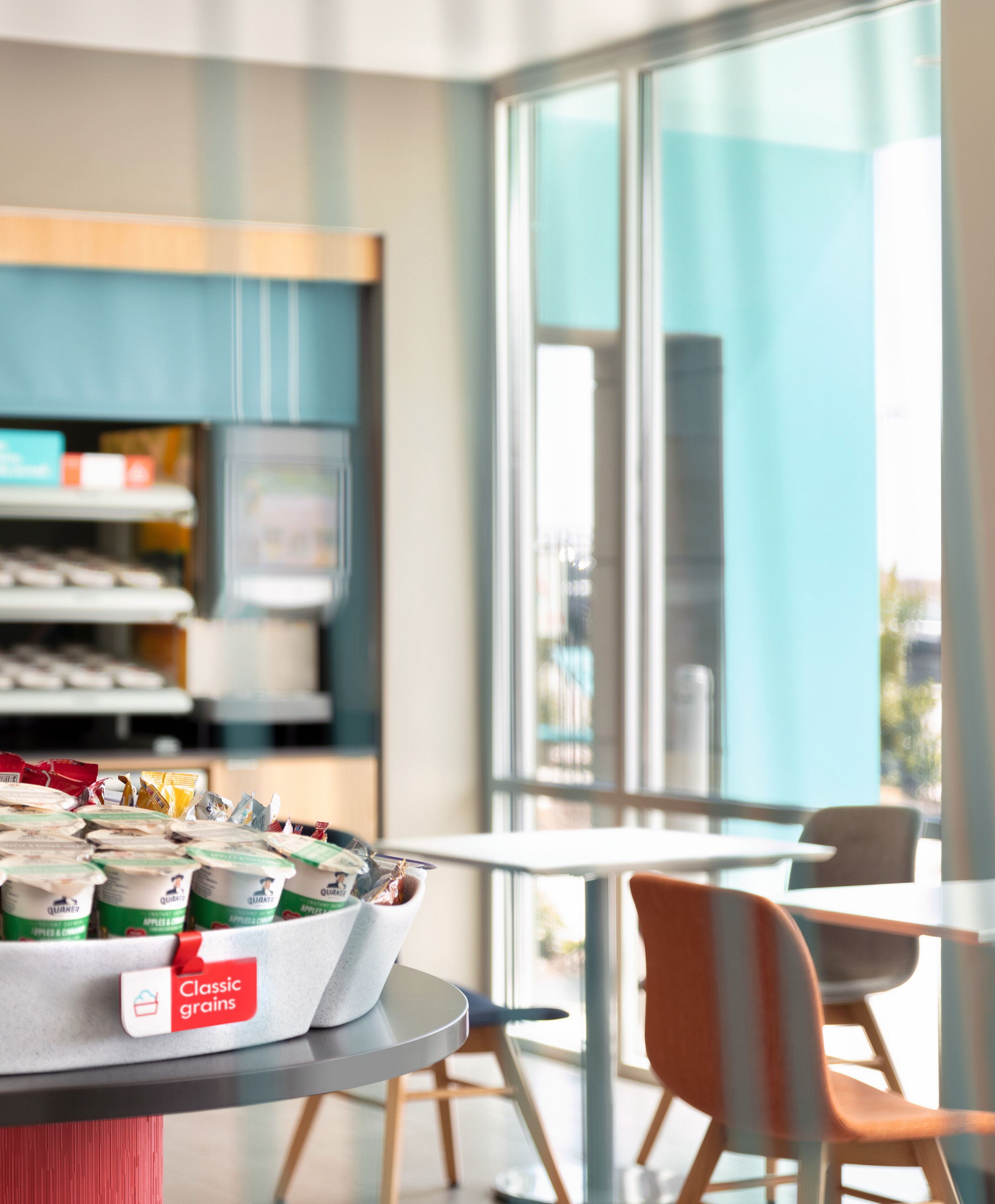 A modern café with a display of yogurt cups labeled "Classic grains" and a view of the city through large windows.