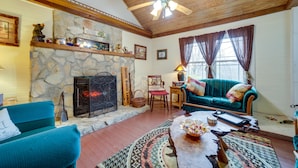 A cozy living room with a stone fireplace, a teal sofa, and a wooden ceiling fan. - Pet-Friendly Smoky Mountain Getaway w/ Fire Pit! (Clyde)