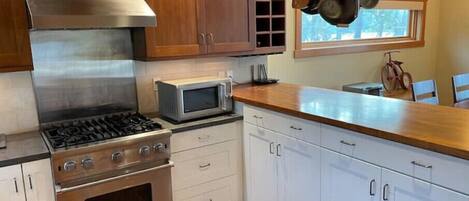 A kitchen with wooden cabinets, a stainless steel stove, a microwave, and hanging pots.