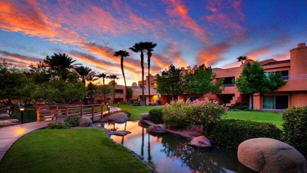 A resort with a swimming pool, palm trees, and a sunset view.