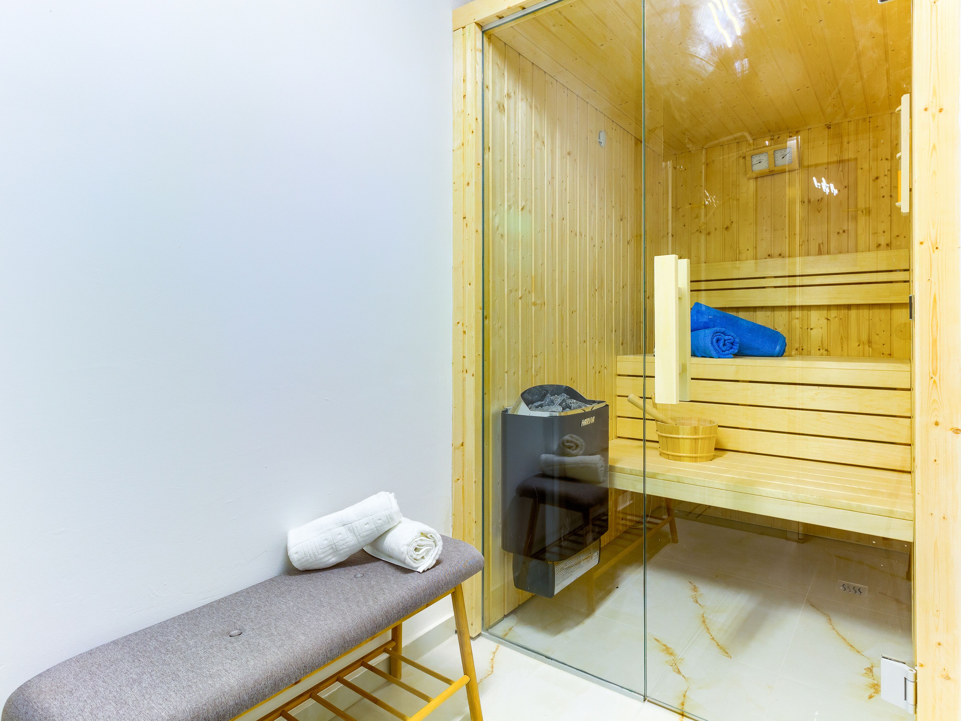 Uma sala de sauna com bancos de madeira, um banco com toalhas, um aquecedor de sauna e um balde de madeira.