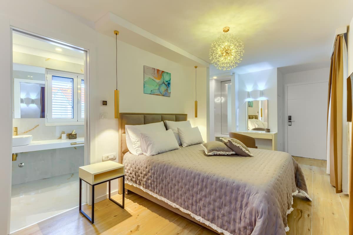A modern bedroom with a large bed, bedside tables, a vanity, and a chandelier.