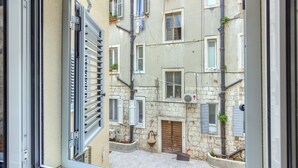 A view through a window of a narrow street with stone buildings, shutters, and a small courtyard. - Irini Luxury Rooms (Split)