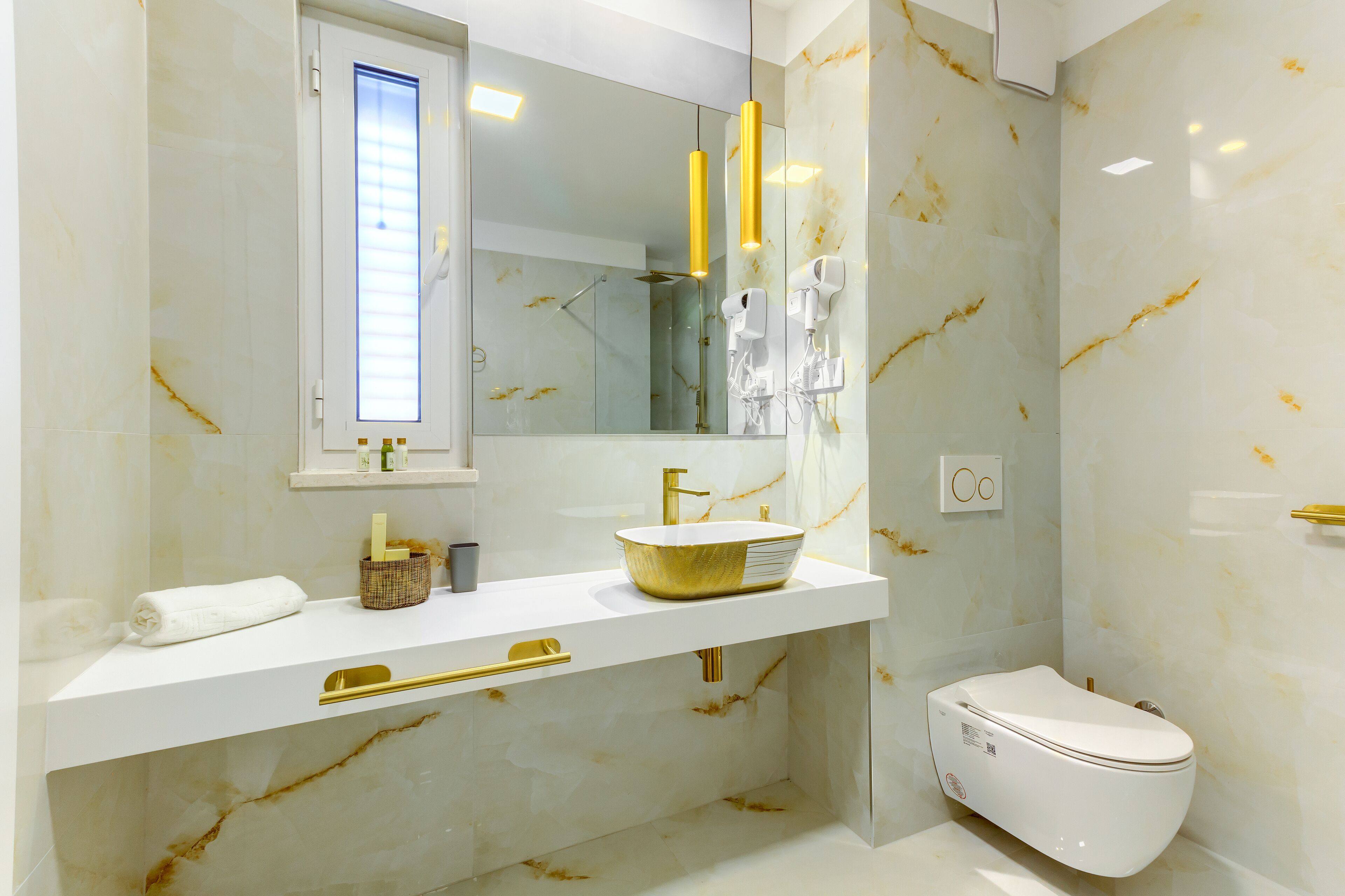 A modern bathroom with a white marble sink, gold fixtures, and a toilet.