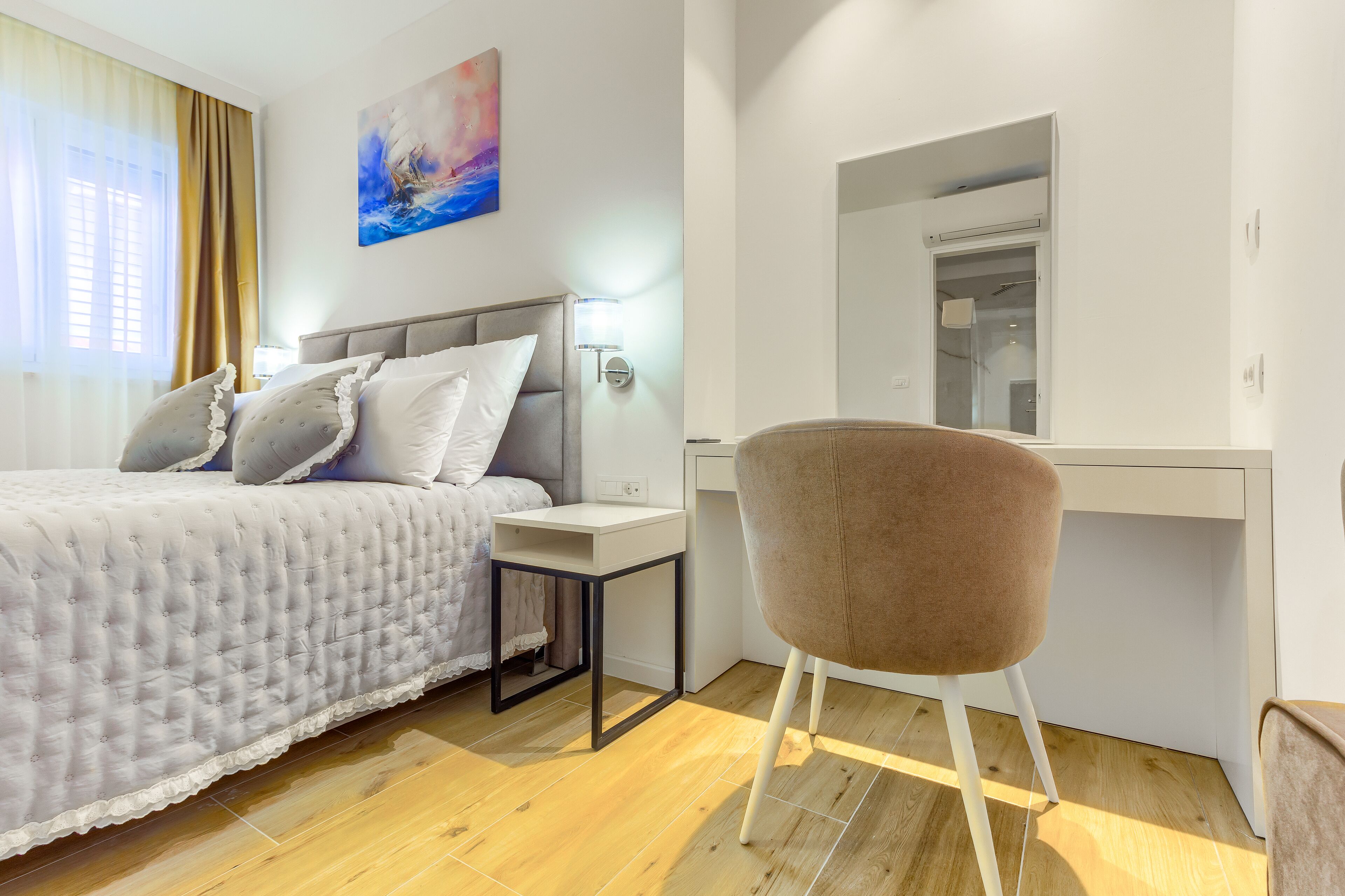 A bedroom with a bed, bedside table, chair, and a desk with a mirror.