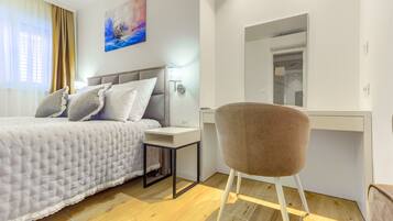 A bedroom with a bed, bedside table, chair, and a desk with a mirror.
