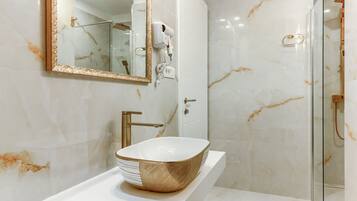 A modern bathroom with a large mirror, a gold-colored vessel sink, a handheld hair dryer, and a glass shower enclosure.