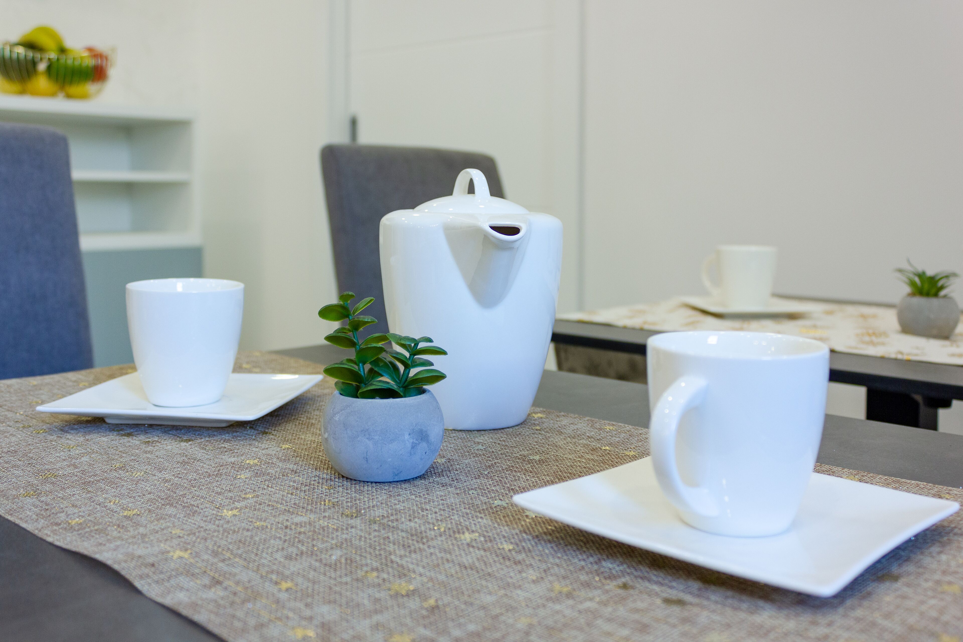 A table with two white cups and a white pitcher on a tablecloth.