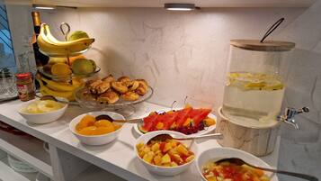 Une table de buffet proposant une variété de fruits, de pâtisseries et un distributeur de boissons.