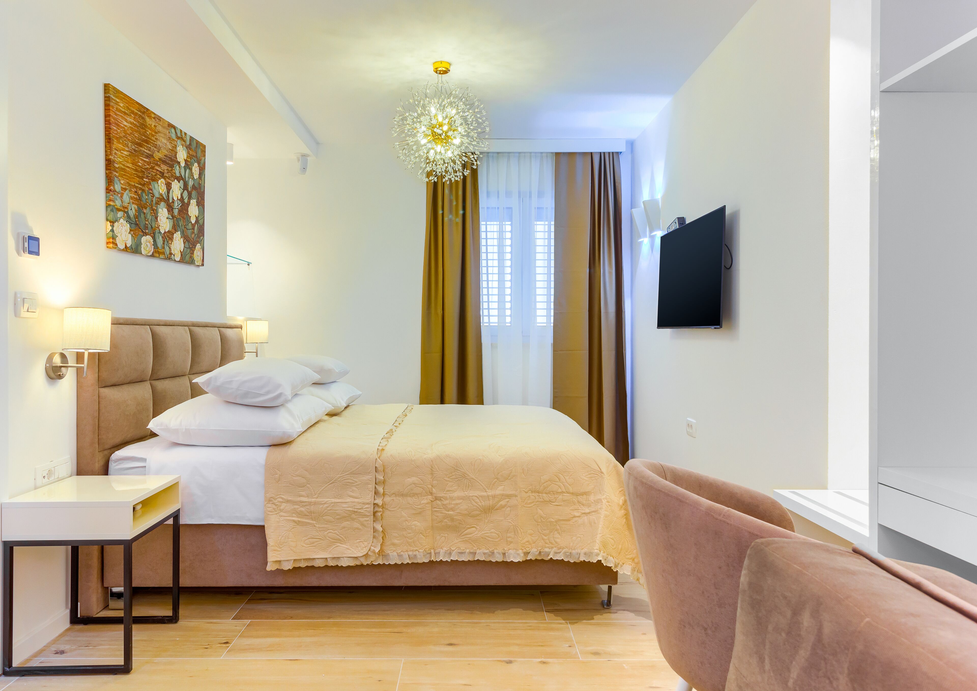 Quarto de hotel com cama, mesa de cabeceira, abajur, televisão e um quadro na parede.