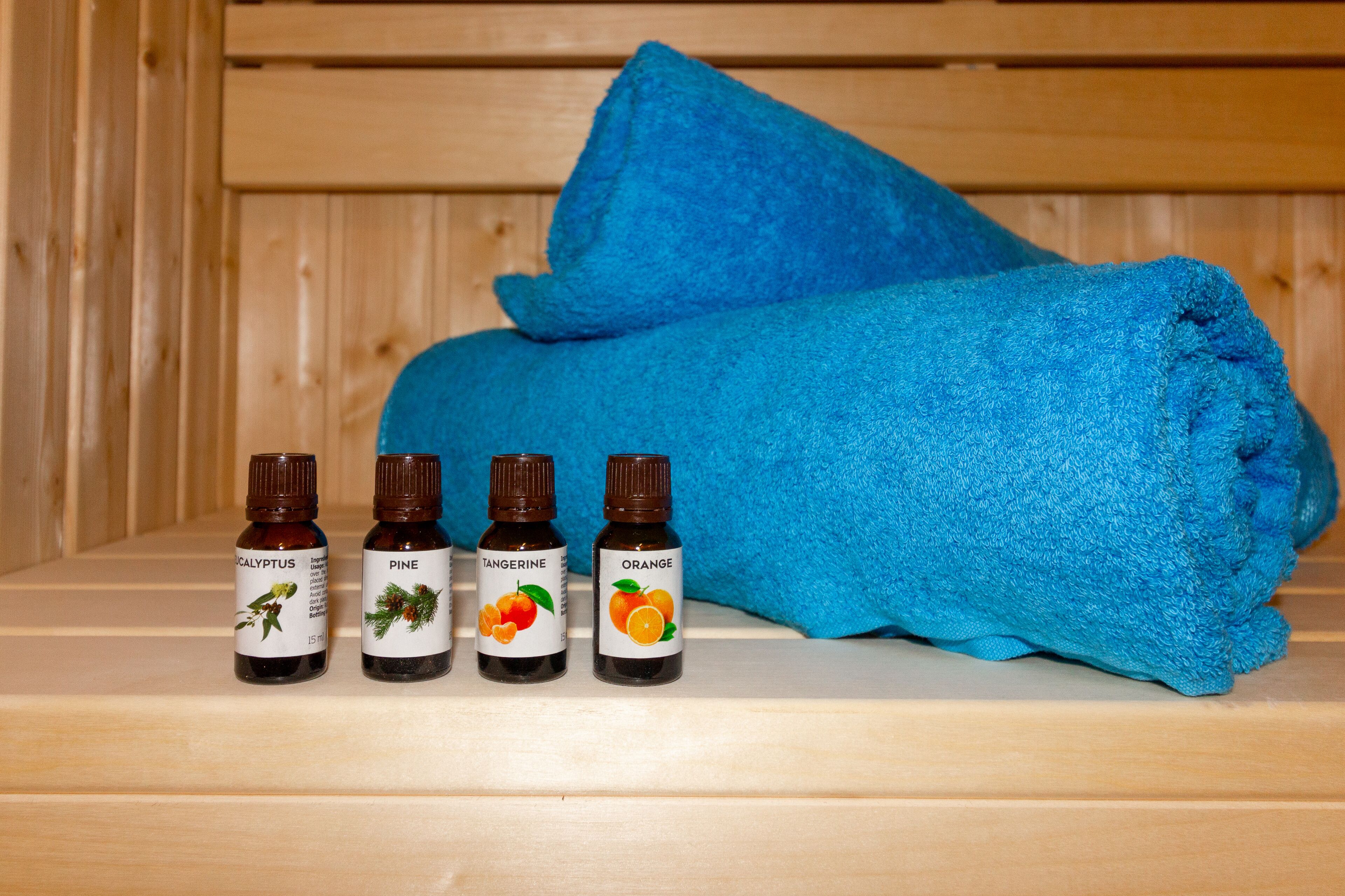A wooden bench with a blue towel and four bottles of essential oils labeled eucalyptus, pine, tangerine, and orange.