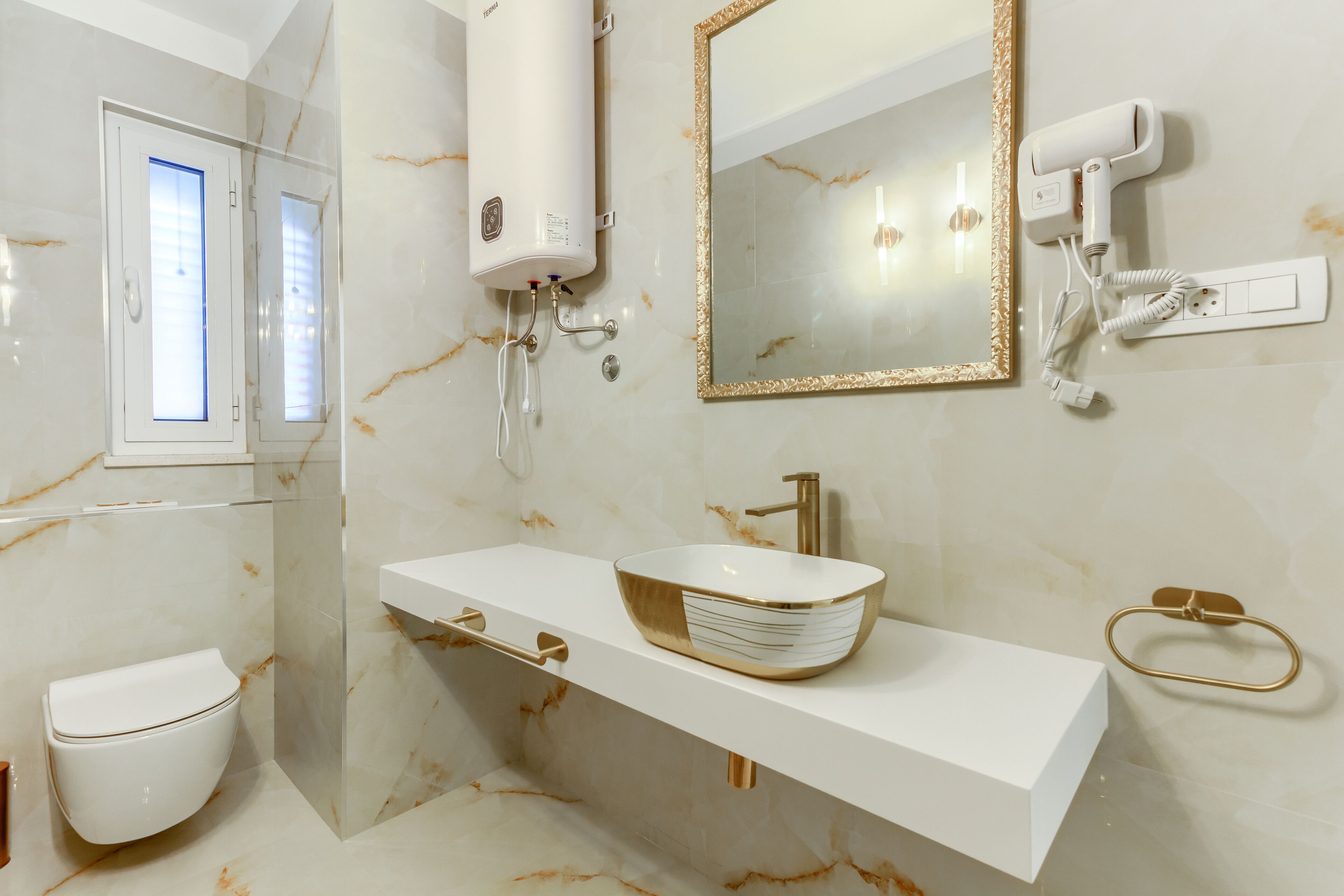A bathroom with a white toilet, a gold and white sink, a mirror with a gold frame, and a towel rack.