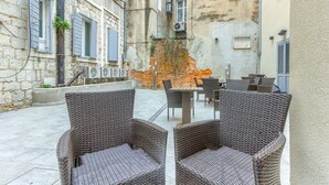A courtyard with wicker furniture, a brick wall, and a stone building. - Irini Luxury Rooms (Split)