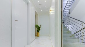 A modern hallway with white walls, a marble floor, a potted plant, and a staircase with metal railings. - Irini Luxury Rooms (Split)