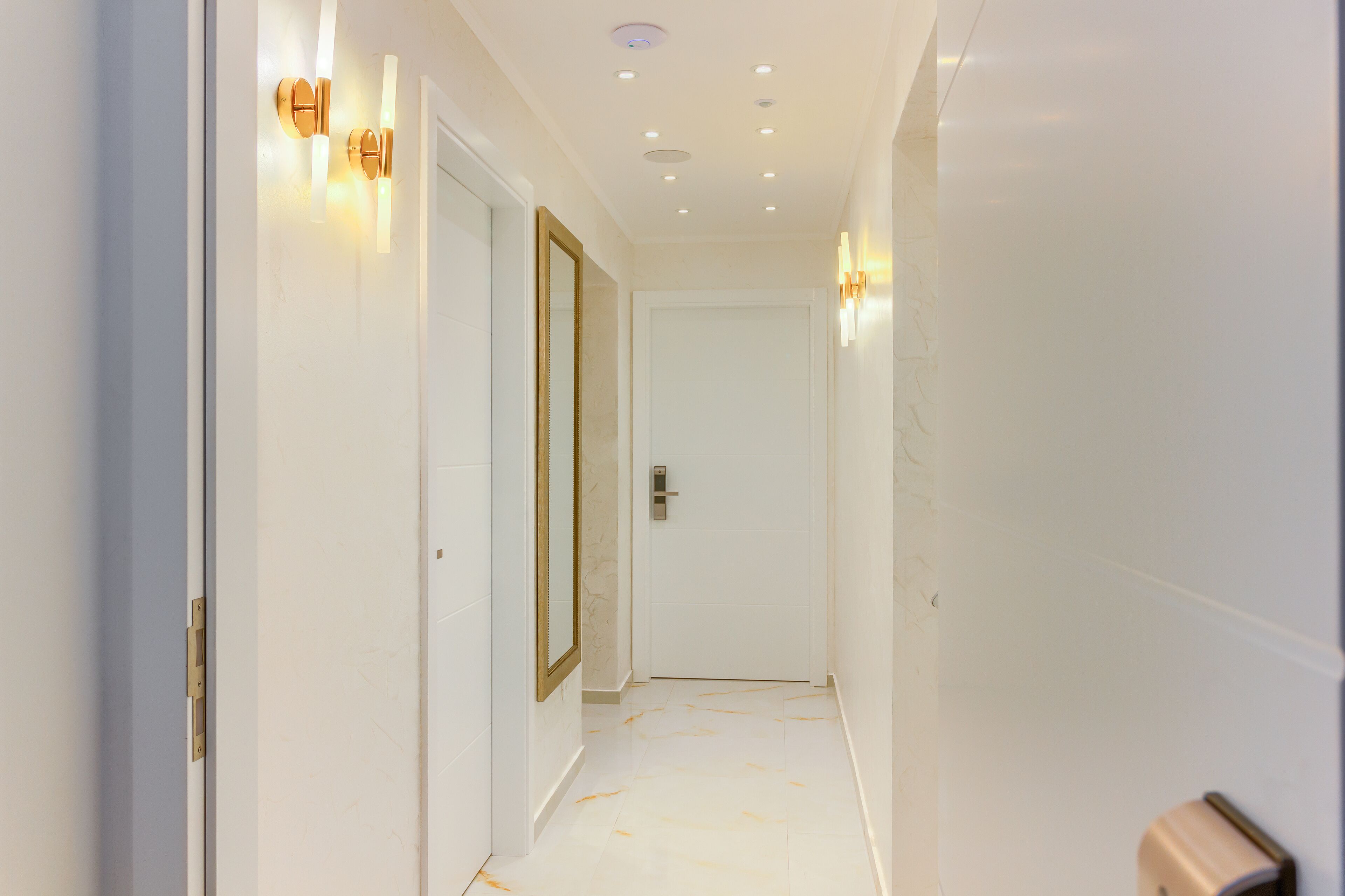 A hallway with white walls, a door with a gold frame, and recessed ceiling lighting.