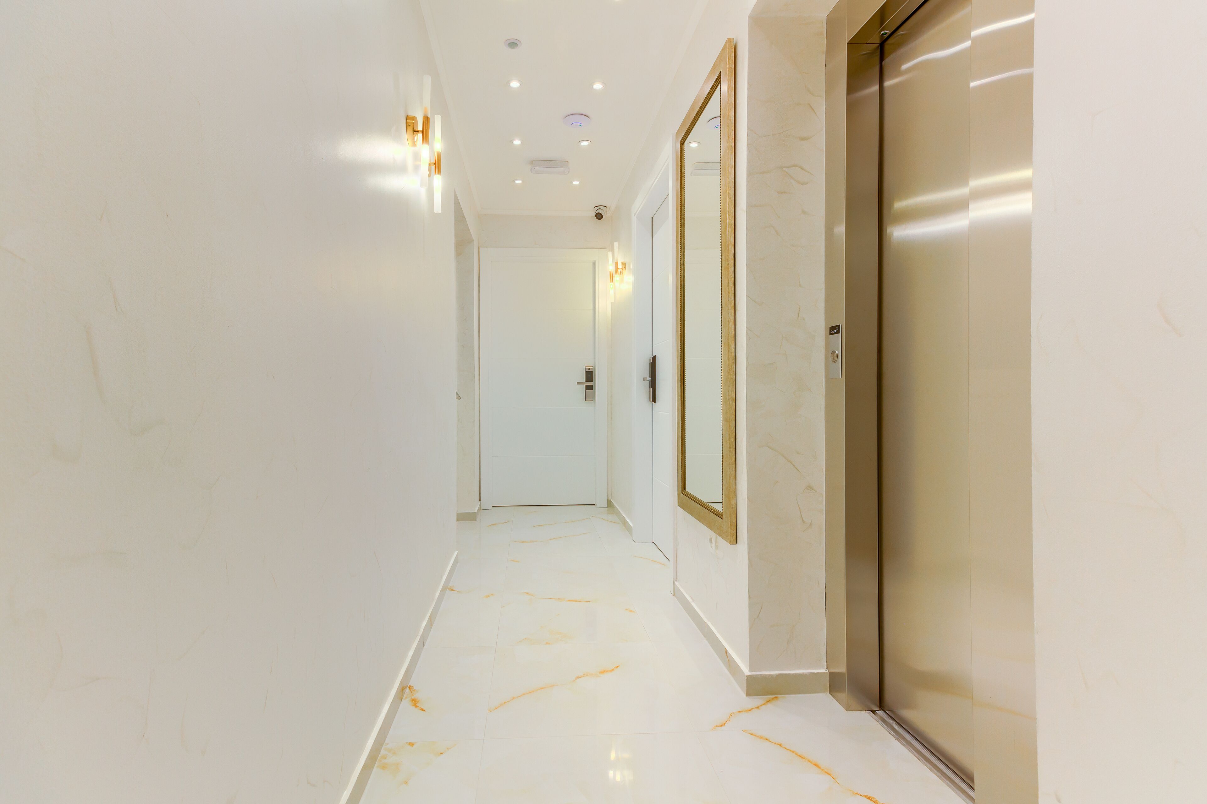 Un pasillo con piso de mármol, un espejo grande y una puerta que da a una habitación.