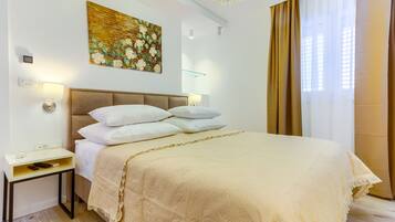 A neatly arranged bedroom with a large bed, a bedside table, a wall-mounted lamp, and a painting above the bed.