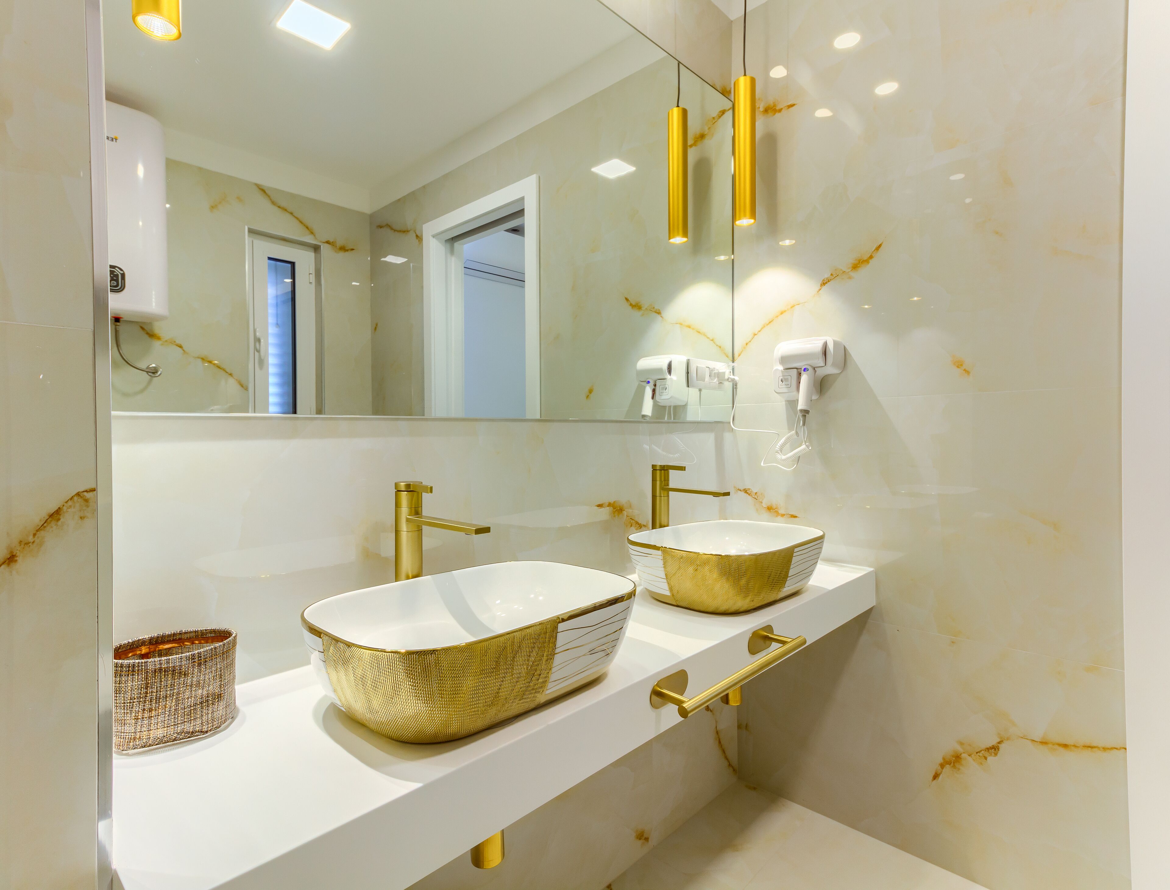 Un baño con dos lavamanos, detalles dorados y un espejo grande.