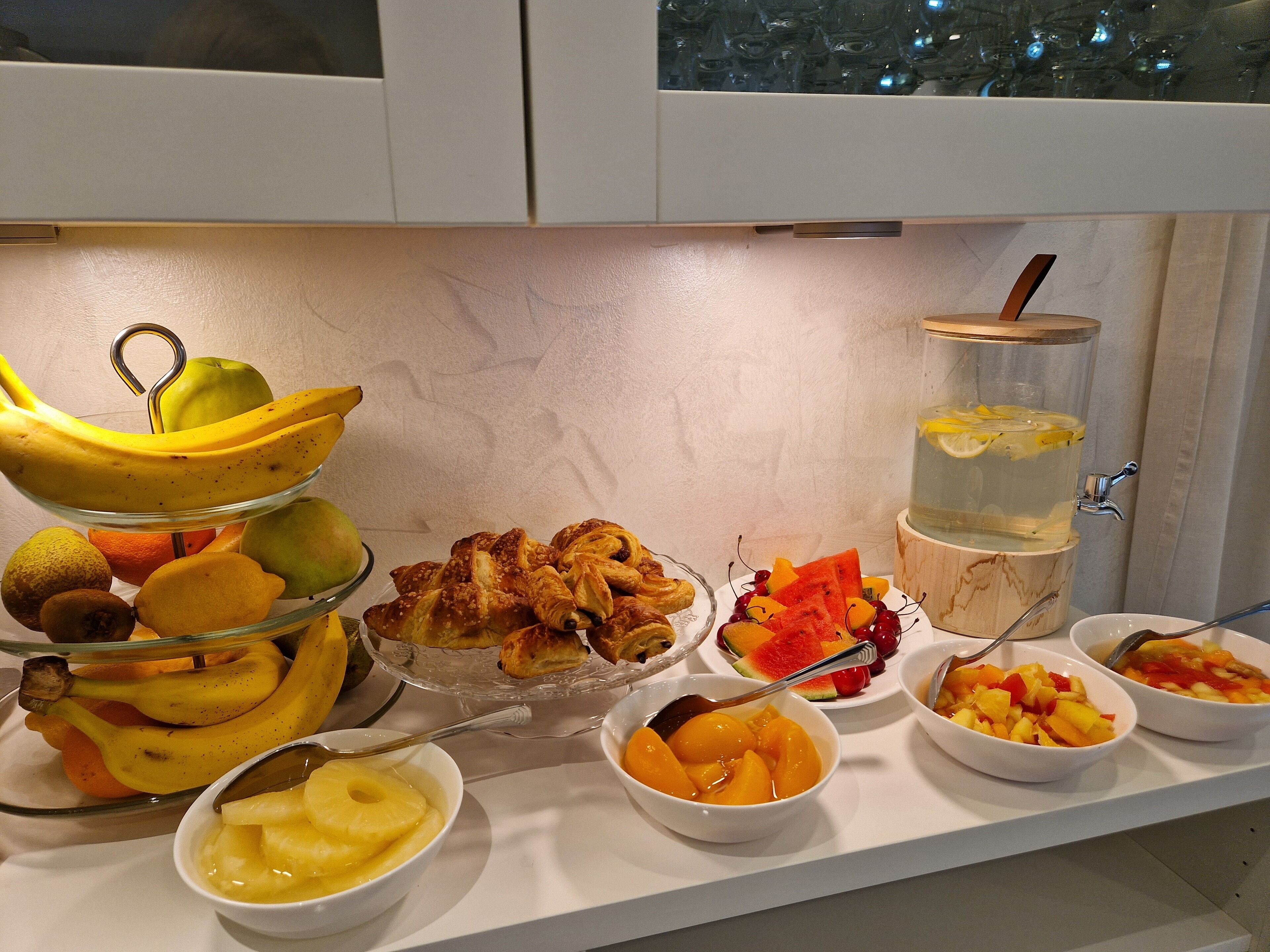 A buffet with various fruits, pastries, and a beverage dispenser.