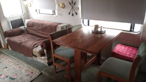 Ein kompaktes Wohnmobil-Interieur mit Holztisch, zwei Stühlen, einer gepolsterten Sitzbank und einem kleinen Fenster.