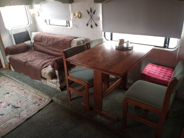A compact RV interior with a wooden table, two chairs, a cushioned sofa, and a small window.