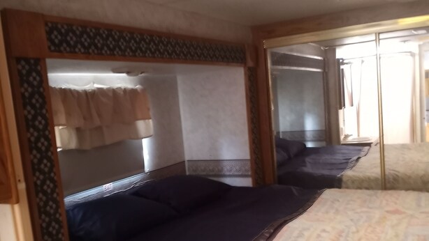 Ein kompaktes Schlafzimmer in einem Wohnmobil, ausgestattet mit einem Bett, einer kleinen Kommode und einem Spiegel.