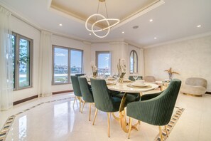 Een eetruimte met een ronde tafel, groene fauteuils en een moderne kroonluchter.