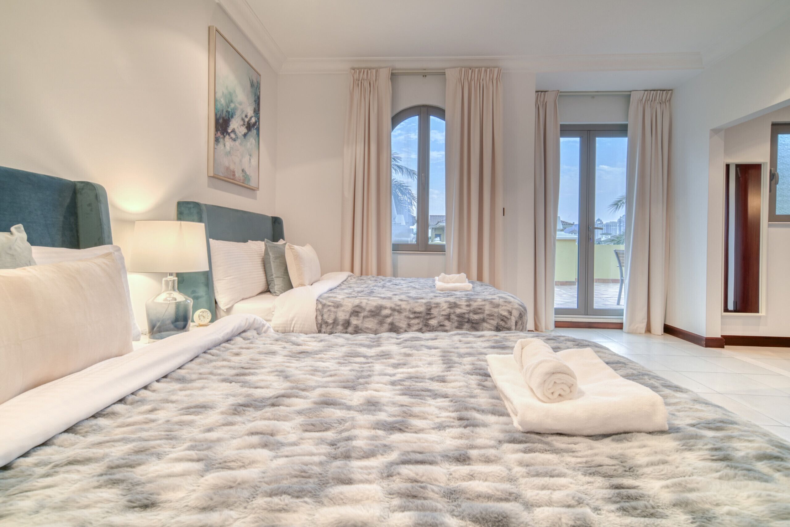 Habitación de hotel con una cama grande, dos mesitas de noche, un ventanal con cortinas y vistas al exterior.