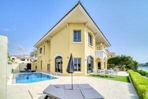 A yellow villa with a swimming pool, outdoor seating, and a view of the sea.