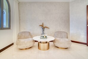 Une pièce comprenant une table ronde en marbre, deux fauteuils rembourrés et un vase contenant des plantes séchées.