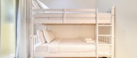 Un lit superposé avec une literie et des oreillers blancs, une fenêtre avec des rideaux et un tapis beige.