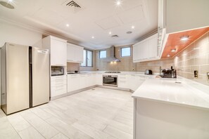 Une cuisine moderne avec des meubles blancs, un four encastré et un grand îlot central doté d’un évier.