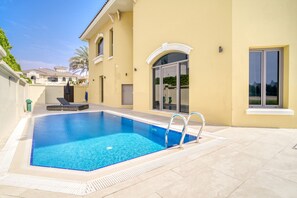Une piscine à l’eau d’un bleu limpide, entourée d’une terrasse carrelée et d’un bâtiment jaune doté de grandes fenêtres et d’une porte.