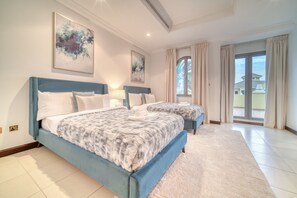 A bedroom with two beds, a large window with curtains, and artwork on the walls.
