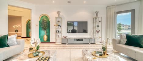 Un salon spacieux avec des tables basses en marbre, un grand téléviseur à écran plat et une vue sur l’extérieur.