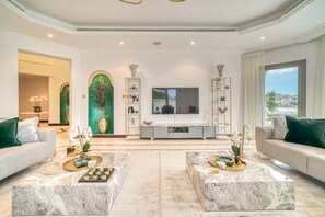 Een ruime woonkamer met marmeren salontafels, een grote flatscreen televisie en uitzicht op de omgeving.