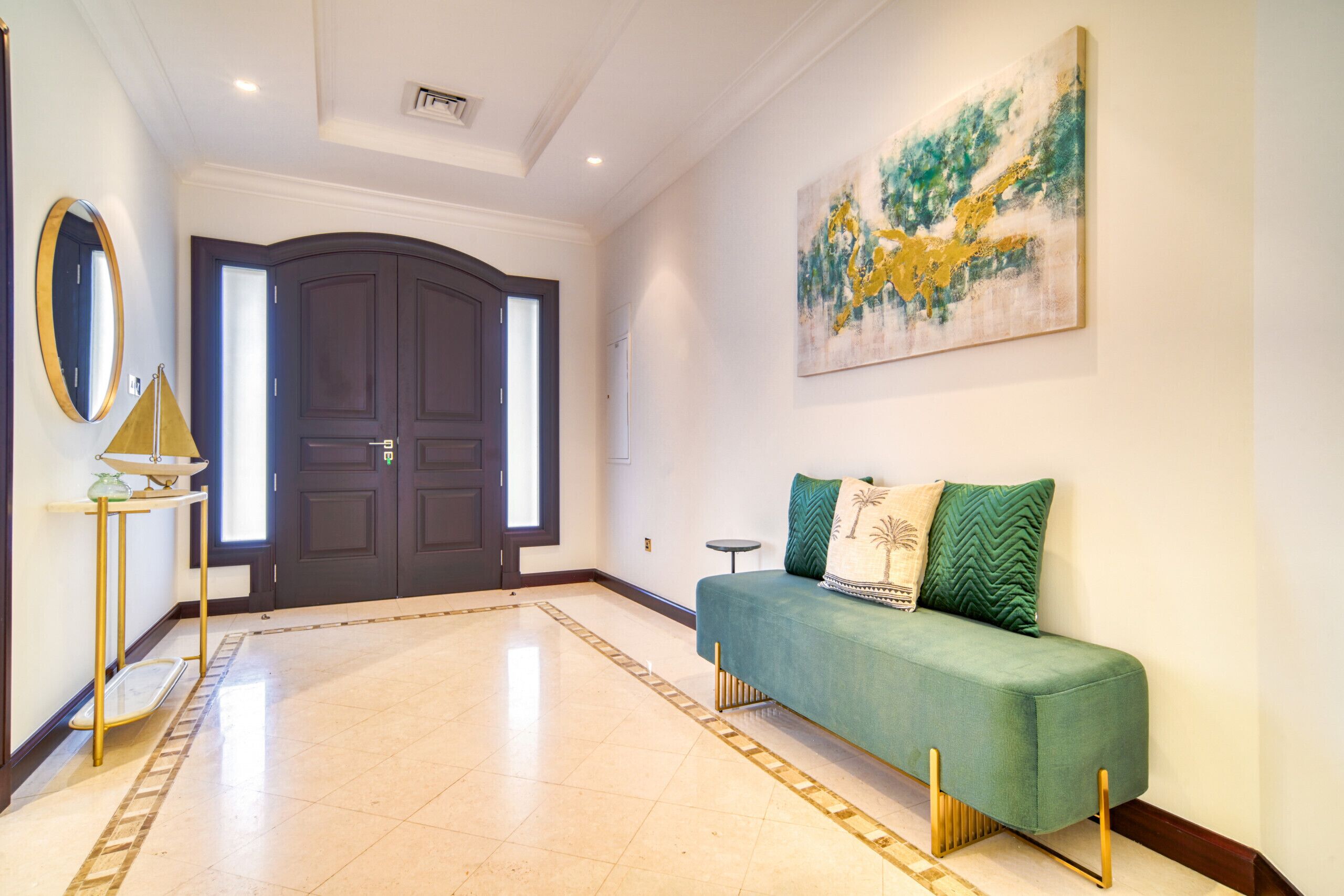 Un'ampia sala con una porta in legno scuro, un divano verde con cuscini decorativi, un piccolo tavolino rotondo e un quadro astratto appeso al muro.