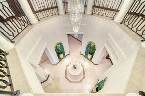 A grand lobby with a central octagonal table, white walls, and a chandelier.