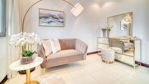 Ett modernt vardagsrum med en beige soffa, ett runt soffbord, en spegel med guldfärgad ram och en vit golvlampa.