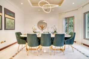 A dining area with a round table, six green upholstered chairs with gold legs, and a modern pendant light. - Beachfront 5BR Villa w/ Private Pool at the Palm (Dubai)