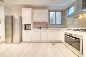 A modern kitchen with white cabinets, a stainless steel refrigerator, a gas stove, and a window above the sink.
