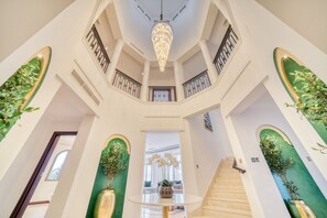 A grand staircase with a chandelier, surrounded by green walls and potted plants.