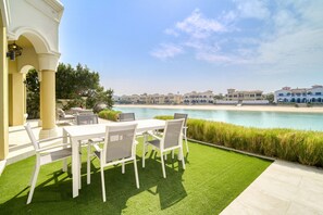 Une terrasse avec une table et des chaises blanches, donnant sur une piscine et des bâtiments.