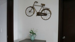 En cykeldekoration på væggen over en grå hylde med en turkis vandkande og en potteplante.