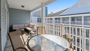 A covered outdoor seating area with a round table and chairs, a sofa, and a view of a building with multiple balconies. - bees knees (Myrtle Beach)
