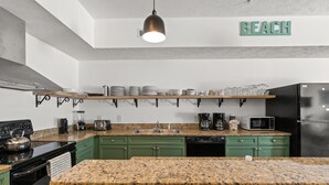 A modern kitchen with granite countertops, green cabinets, a black refrigerator, and a 'BEACH' sign on the wall. - bees knees (Myrtle Beach)