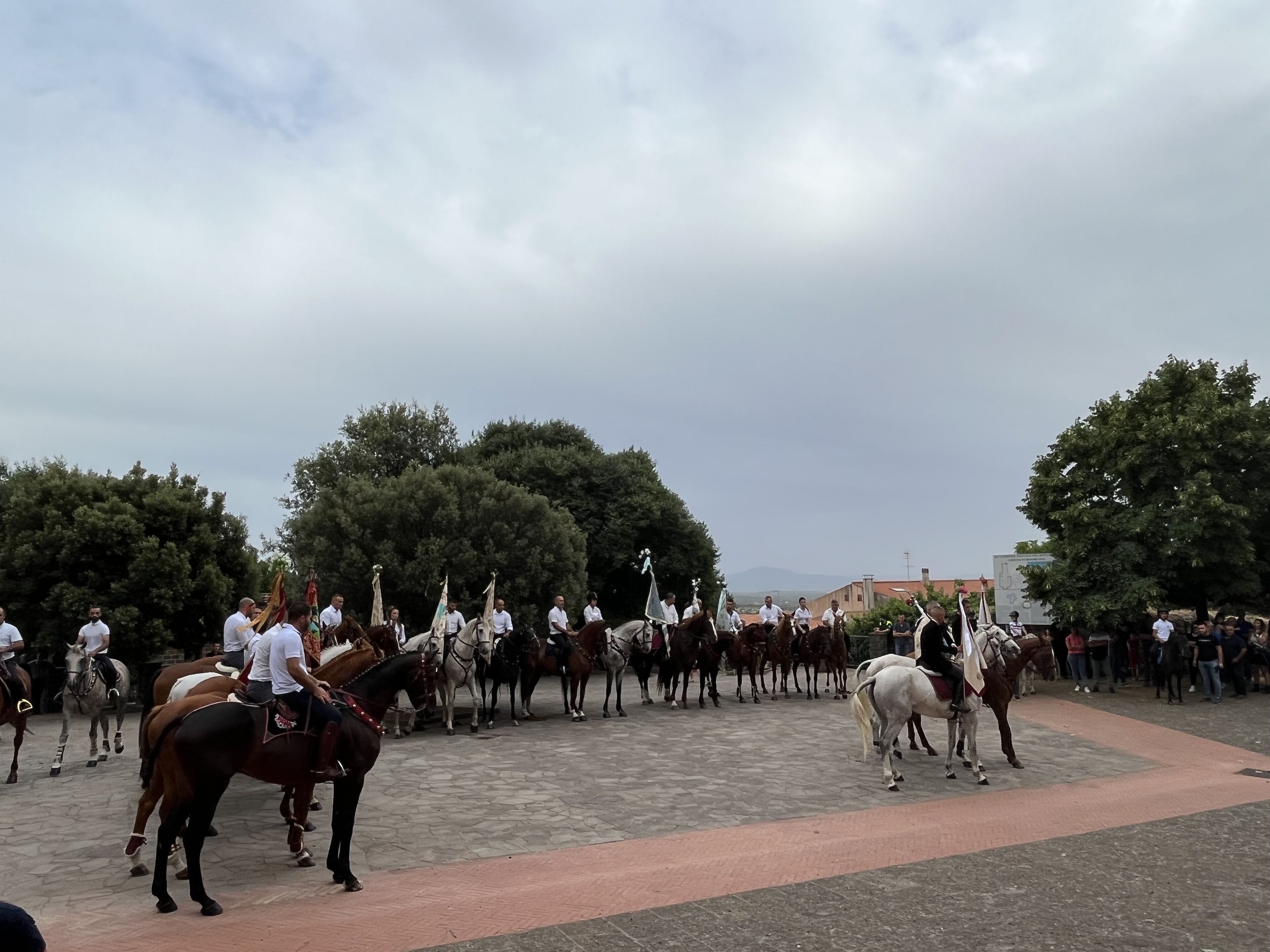 Un groupe de personnes à cheval, dans un cadre extérieur, avec des arbres et des bâtiments en arrière-plan.