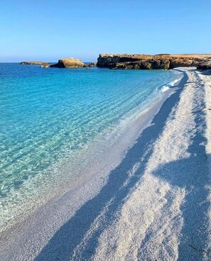A beach with clear turquoise water, sandy shore, and rocky cliffs in the background. - HOUSE SEA MOUNTAIN (Bonarcado)